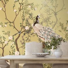 a peacock sitting on top of a wooden table next to a vase filled with flowers