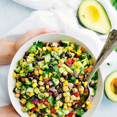 a person holding a bowl of salad with avocado and black beans on the side