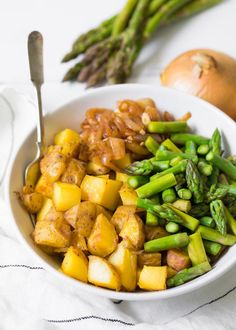 a white bowl filled with asparagus, potatoes and other food on top of a table