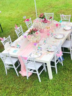 an outdoor table set up with pink and white flowers in vases, plates and napkins