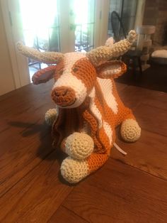 a crocheted cow laying on top of a wooden floor