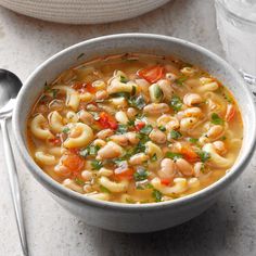 a white bowl filled with pasta and vegetables next to silverware on a marble table