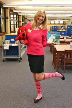 a woman in a pink sweater and black skirt holding a red teddy bear while posing for the camera