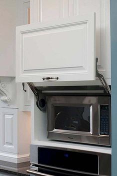 a microwave built into the side of a kitchen wall with white cabinets and cupboards