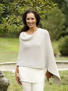 a woman standing in front of a tree wearing a white sweater and pant suit