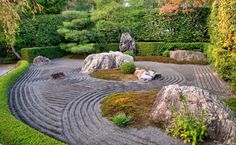 a garden with rocks and plants in the center, surrounded by green bushes on either side