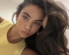 a woman with long brown hair is wearing a yellow shirt and posing for the camera