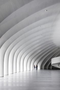 two people are standing in the middle of an empty room with white walls and arches