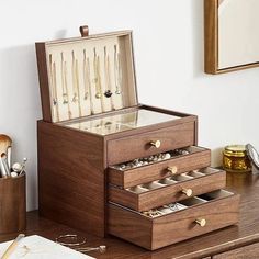 an open wooden jewelry box sitting on top of a desk next to a pen and pencil holder