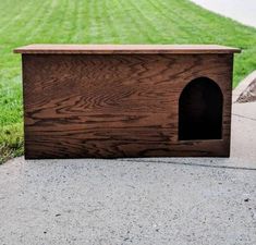 a wooden dog house sitting on the side of a sidewalk next to a grass field