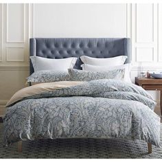 a bed with blue and white comforter in a bedroom next to a nightstand on top of a table