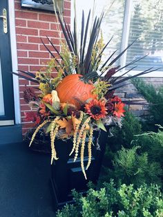 an arrangement of fall flowers and pumpkins in a planter