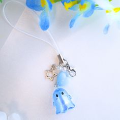 a blue elephant keychain with a star charm on it's side and flowers in the background