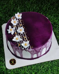 a purple cake sitting on top of a green field covered in grass with flowers and pearls