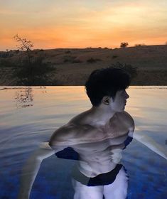 a man is standing in the water with his shirt off and looking at the sky