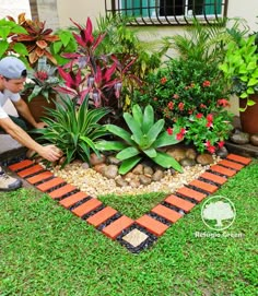 a man kneeling down next to a garden filled with plants and rocks in front of a house