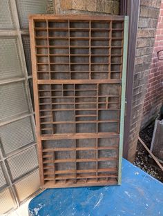 an old wooden bookcase sitting on top of a blue table next to a brick wall