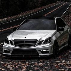 a silver car parked on the side of a road next to some trees and leaves