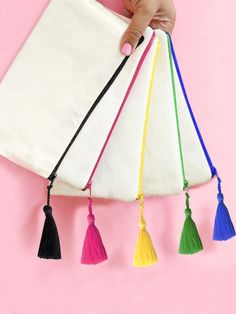 a hand holding a white bag with tassels on it and five colors of the same color