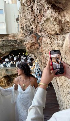 a woman taking a photo with her cell phone while standing next to a rock formation