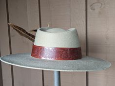 The Melinda felt hat is 100% wool and has a stiff 4" brim and 4.5" diamond crown. The wide whiskey color leather band has been embossed in a floral pattern. A large Thunderbird Concho with faux turquoise is a striking accent. Finished with pheasant feathers. Note: Hats are made to order. Allow up to 4 weeks for your hat to ship. Flat Crown Felt Hat For Kentucky Derby, Felt Hat For Kentucky Derby With Flat Crown, Artisan Felt Hat With Flat Crown For Kentucky Derby, Artisan Felt Hat With Flat Crown For Rodeo, Artisan Flat Crown Felt Hat For Rodeo, Hat Holder, Cloth Tape, Pheasant Feathers, Diamond Crown