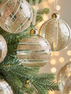 christmas ornaments hanging from a tree with lights in the background