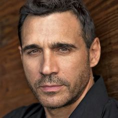 a close up of a person wearing a black shirt and tie with a wooden wall in the background