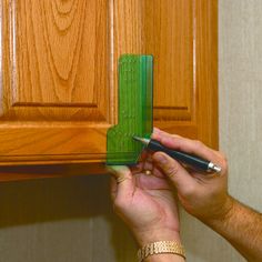 a person is holding a green piece of plastic in front of a wooden cabinet door