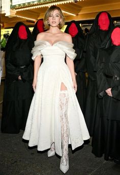 a woman in a white dress standing next to some people wearing black and red costumes