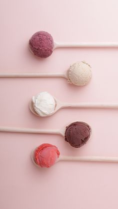 four scoops of ice cream are lined up on a pink surface with three spoons