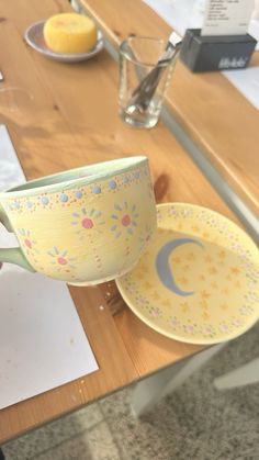 a yellow cup sitting on top of a wooden table next to a plate and bowl