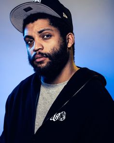 a man with a beard wearing a black jacket and a baseball cap is looking at the camera