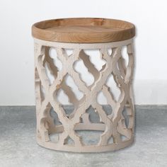 a wooden stool with an intricate design on the top and bottom, sitting on concrete flooring