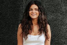 a woman with long hair standing in front of a black wall and smiling at the camera