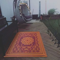 a red rug sitting on top of a wooden floor next to a chair and potted plant