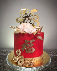 a red cake with gold decorations and flowers on top is sitting on a glass plate