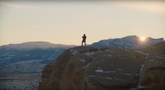 a person standing on top of a mountain with the sun setting behind them and mountains in the background