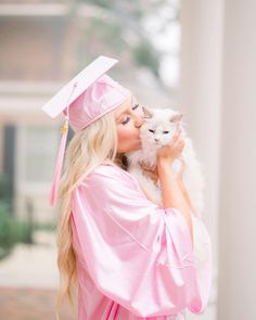 a woman in a pink graduation gown holding a white cat