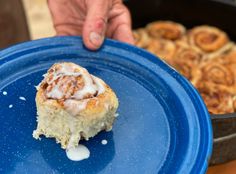 a person holding a blue plate with cinnamon rolls on it