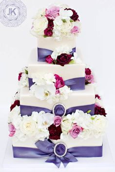 a three tiered wedding cake with purple ribbon and flowers on top is displayed in front of a white background