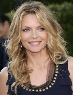 a woman with long blonde hair and blue eyes smiles at the camera while wearing a black dress