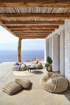 an outdoor covered patio with pillows on the floor and in front of it, looking out at the ocean