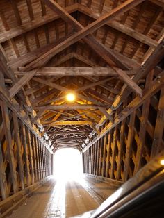 the inside of a wooden covered bridge with sunlight coming in from the ceiling and cars going through it