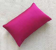 a pink pillow sitting on top of a bed next to a white blanket and pillows