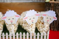 there are three sheep cutouts on the top of some popcorn pop sticks in front of a white picket fence