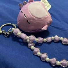 a pink stuffed animal with pearls on a blue blanket next to a keychain