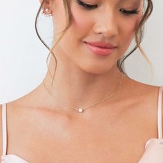 a woman wearing a necklace with a pearl on it