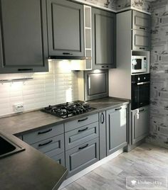 a kitchen with grey cabinets and white walls, an oven and microwave in the corner