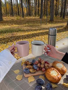 two people sitting at a picnic table with bread, grapes and muffins on it