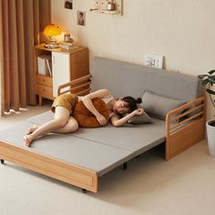 a woman laying on top of a bed next to a plant in a living room